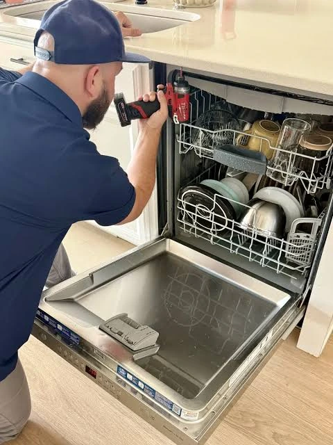 Technician adjusting a dishwasher beneath a kitchen countertop