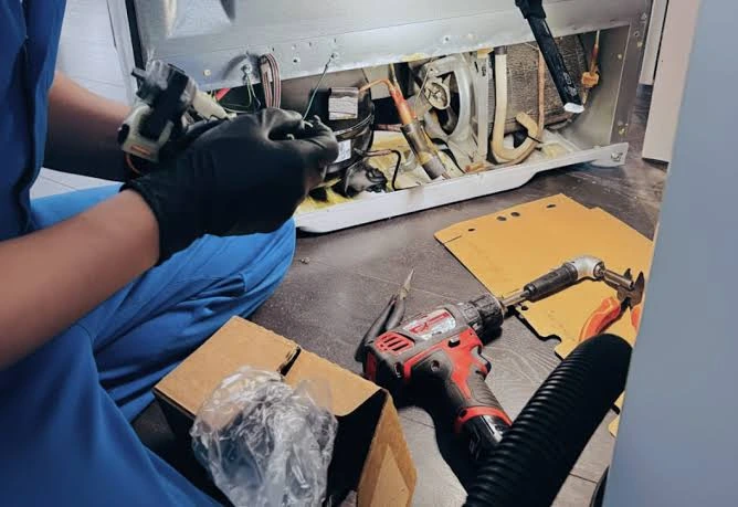 Gloved technician inspecting components beside a refrigerator compressor